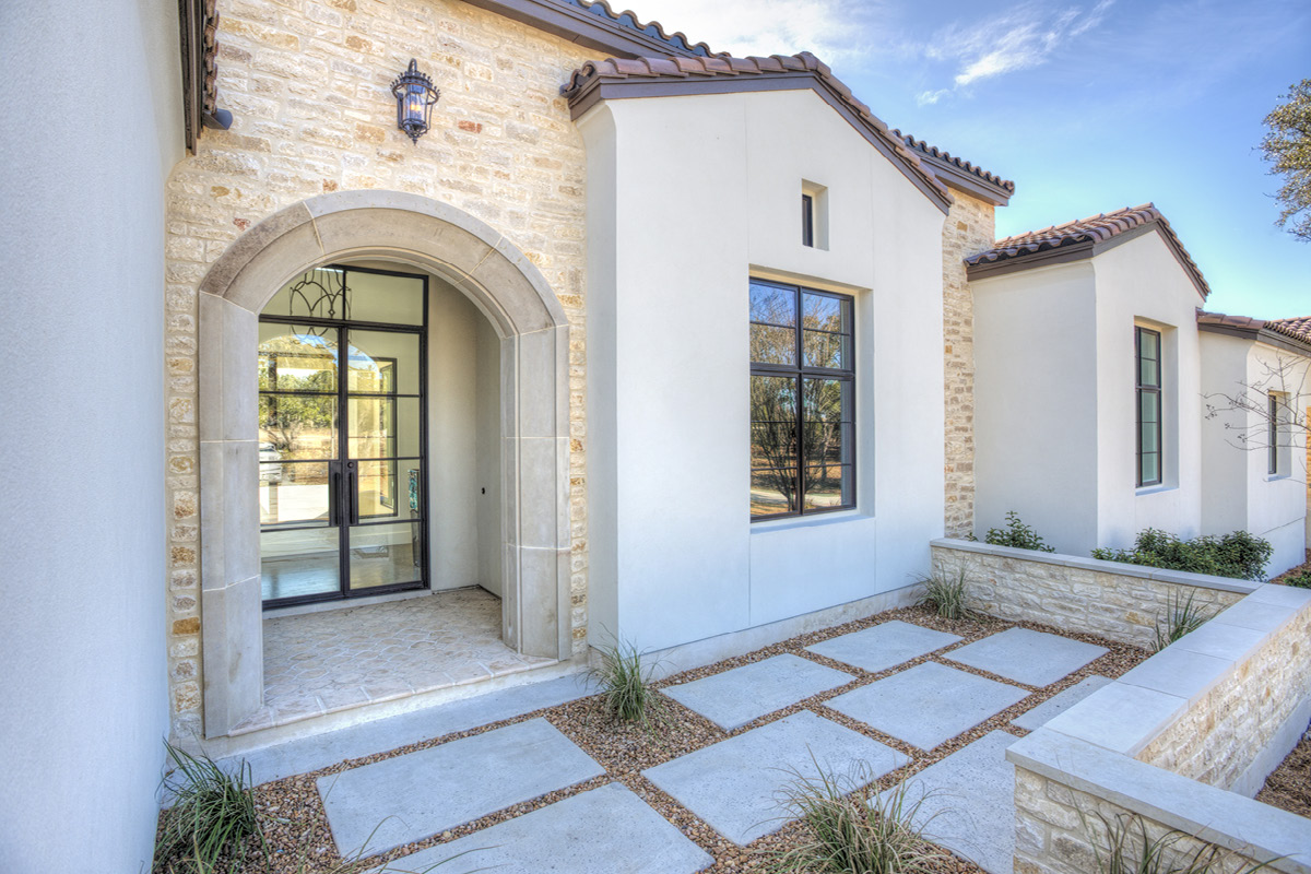 Spanish Revival front entrance with stone archway, wrought iron light fixture, glass front door, and stone walkway leading to entry.