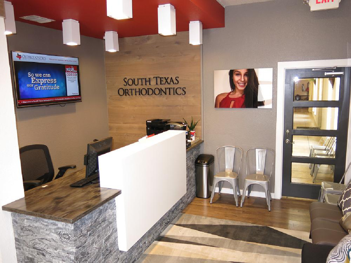 Reception desk at South Texas Orthodontics with stone accents, wood wall signage, and contemporary waiting area.