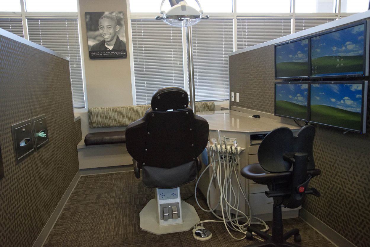 Stone Oak Orthodontics exam room in San Antonio with dental chair, workstation, and multiple wall-mounted monitors.