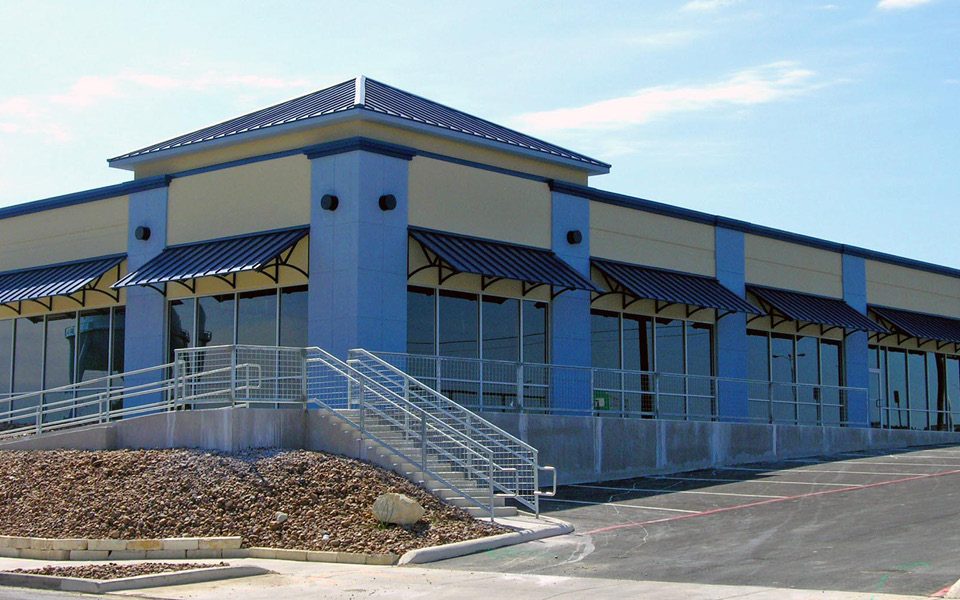 Completed Agora Place retail shell building featuring multiple storefronts, blue awnings, and exterior stair access.