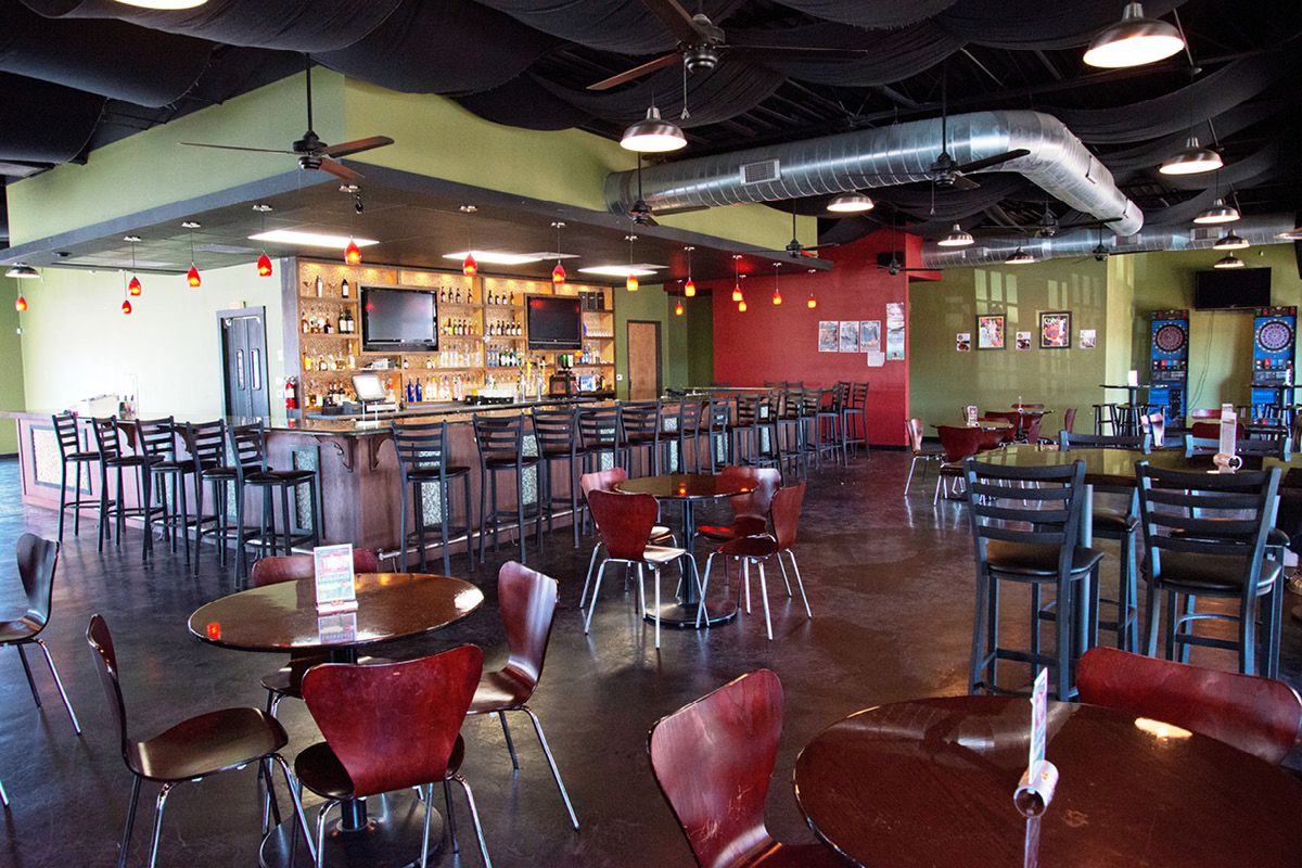 evil olive - Wide shot of Evil Olive interior featuring the bar as focal point, red and green accent walls, and open seating layout.