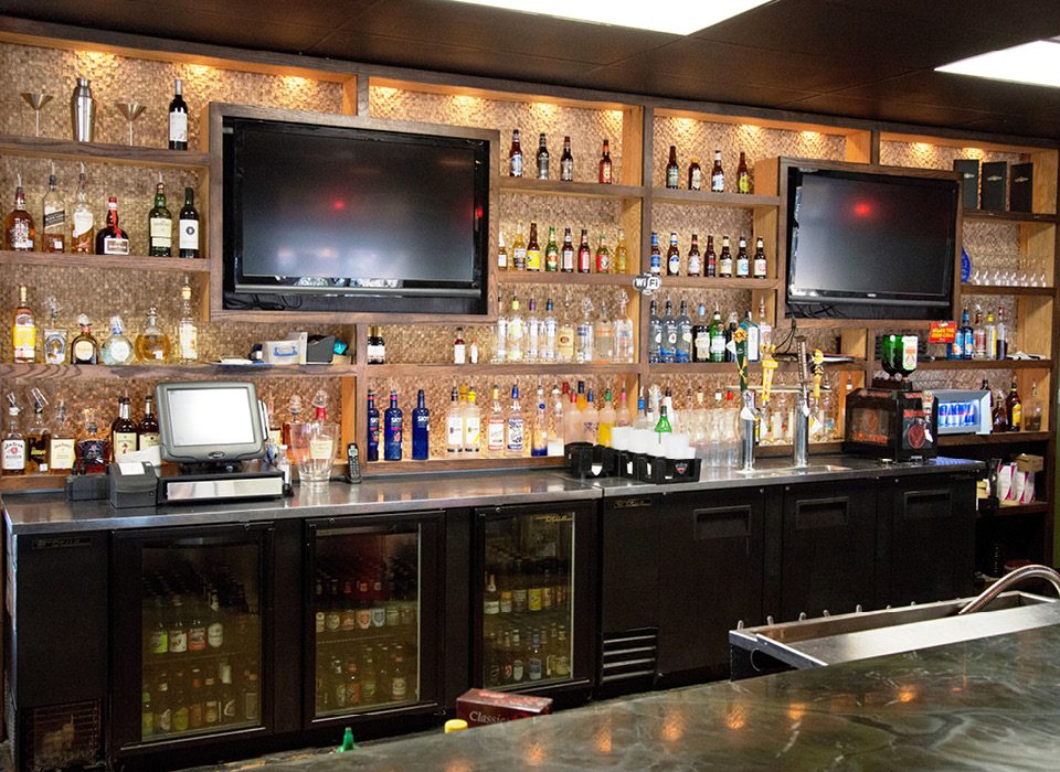 Close-up view of Evil Olive’s bar with liquor shelves, mounted TVs, and illuminated shelving.