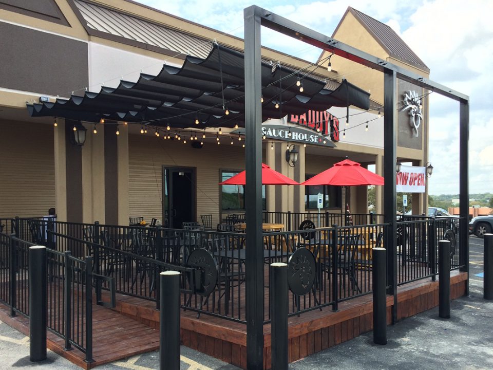 Outdoor patio seating area at Wing Daddy’s restaurant in San Antonio with string lights, red umbrellas, and modern black railing.