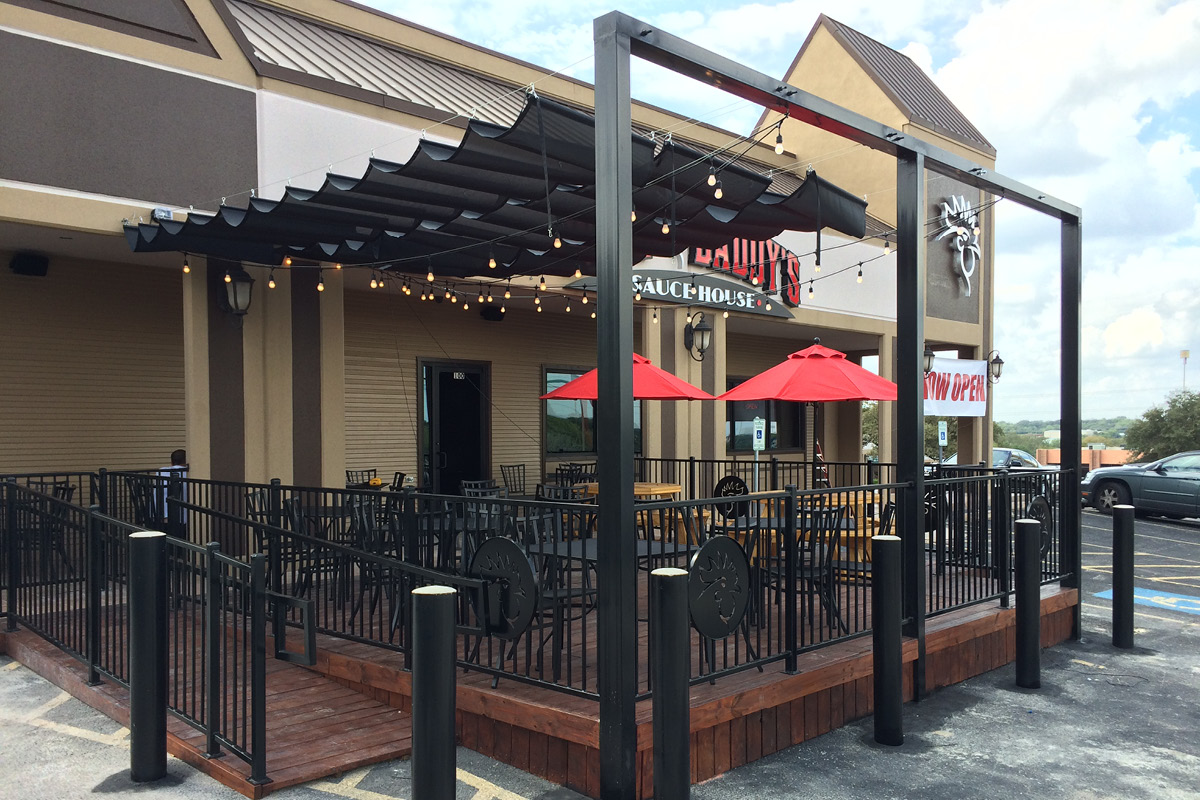 wing daddys2 Outdoor patio seating area at Wing Daddy’s restaurant in San Antonio with string lights, red umbrellas, and modern black railing.