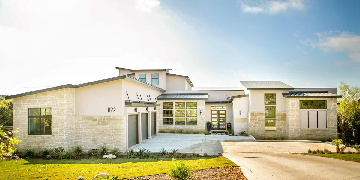 Modern home exterior with stone and stucco design, flat rooflines, three-car garage, and large glass entry door.