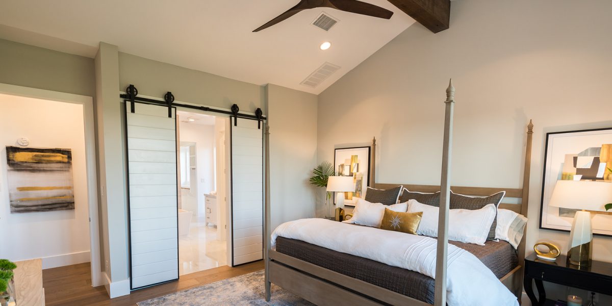3674-9 Cozy bedroom with a four-poster bed, vaulted ceiling with wood beam, and sliding barn doors leading to the ensuite bathroom.