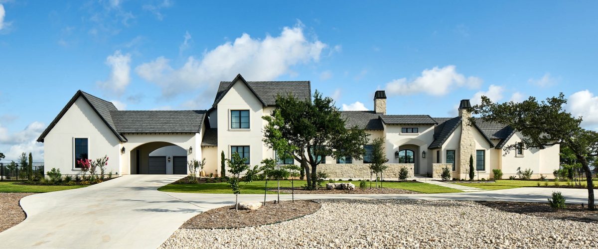 Timeless French Country exterior with stone façade, pitched roofs, and classic arched doorway