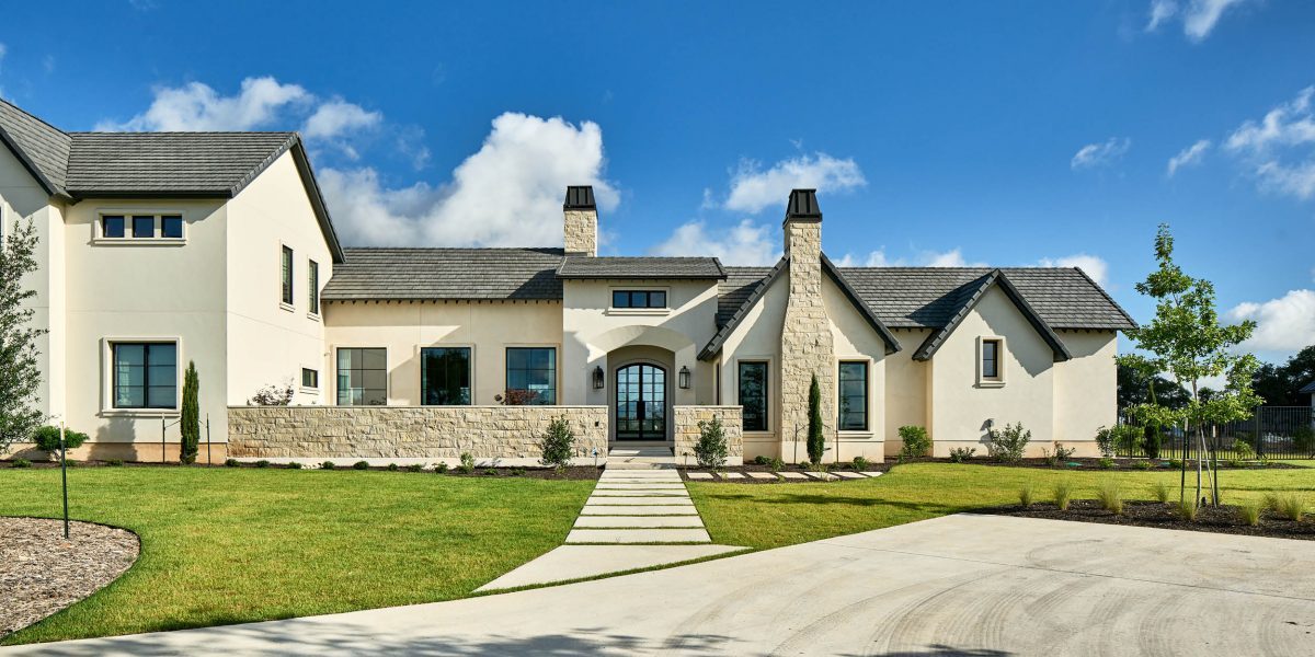 Elegant French Country style home with light stucco exterior, stone chimneys, and arched front entry