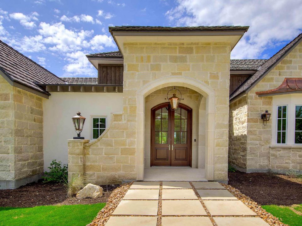 Luxury French Country home designed by MSA Architecture + Interiors featuring stone exterior and arched entryway