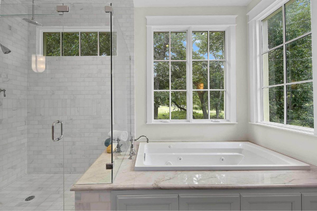 Elegant master bathroom featuring glass shower, marble finishes, and spa-like soaking tub with natural light