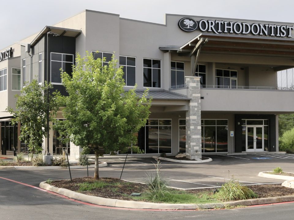 Exterior view of Norris MOB, a modern two-story medical office building in San Antonio with orthodontist signage, large windows, and stone accents.