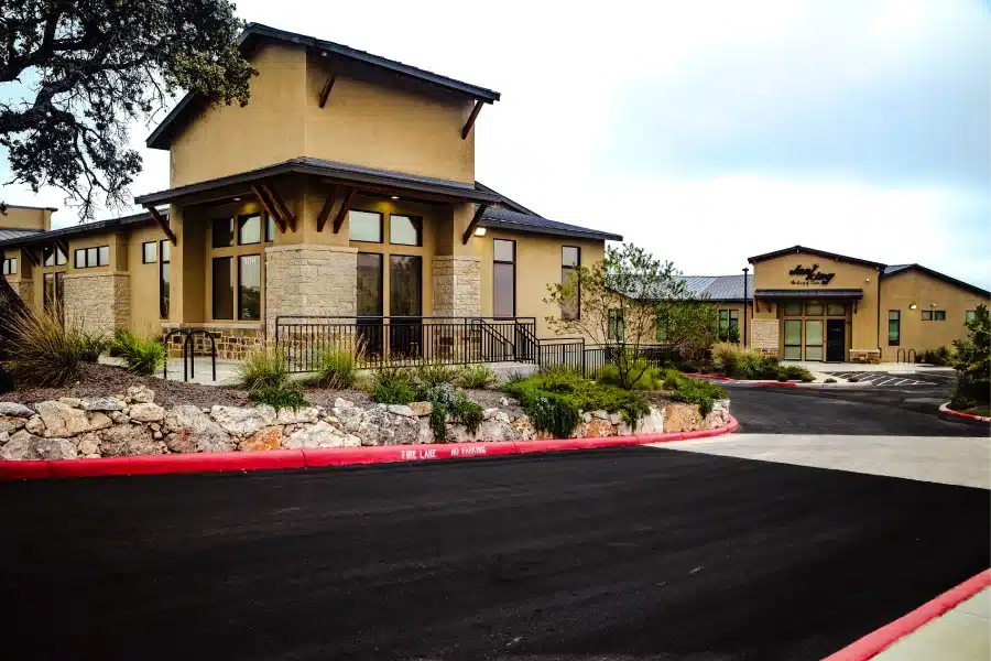 Modern commercial building designed by MSA Architecture + Interiors, featuring stone columns, timber accents, large glass entry doors, and a metal roof under a bright blue sky.