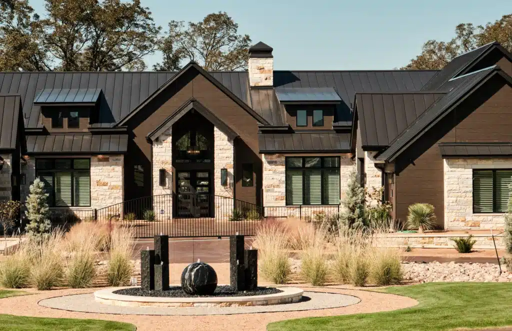 Modern luxury home in San Antonio designed by MSA Architecture + Interiors featuring stone exterior, black metal roof, and landscaped front courtyard fountain on Legends Parkway